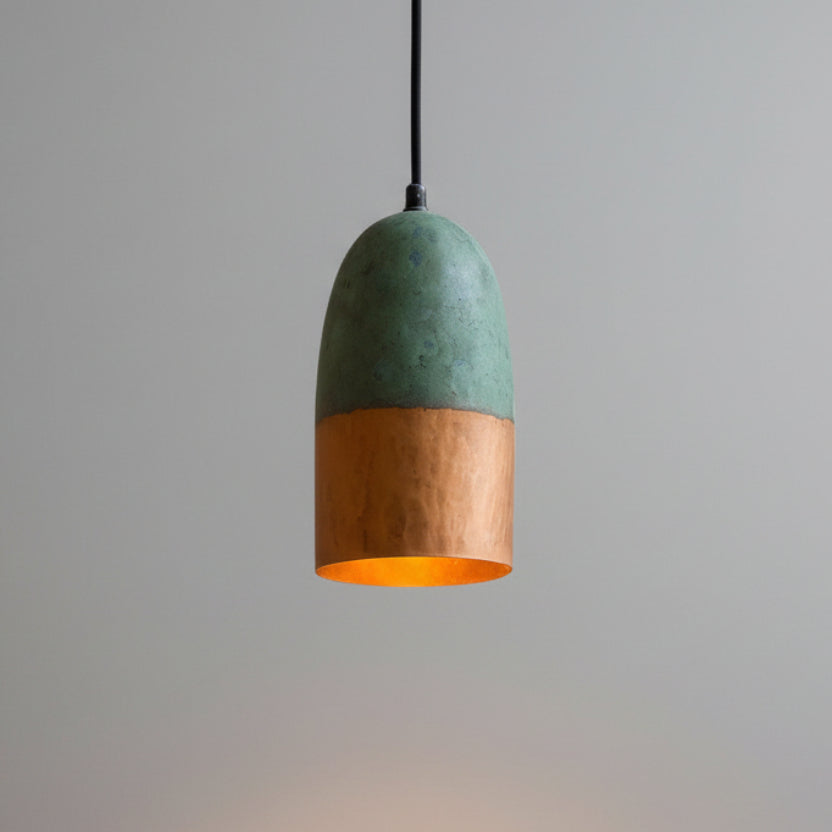 A modern pendant light with a green and orange color scheme hangs from the ceiling against a textured beige wall.