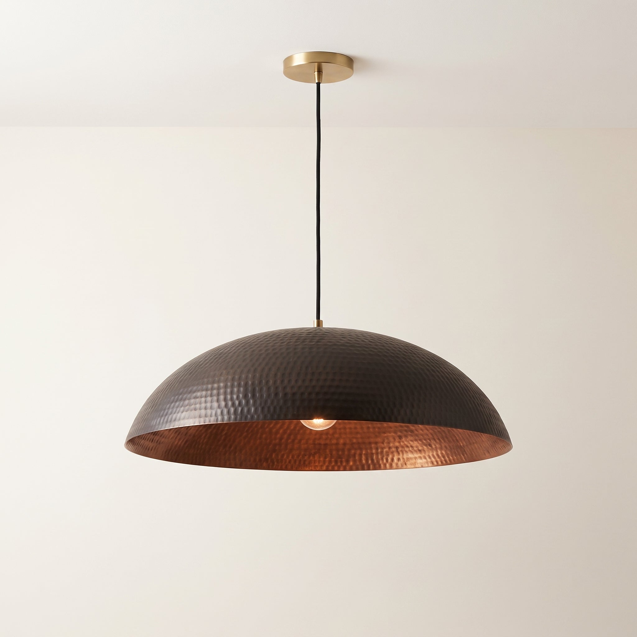 Black copper pendant light with wide hammered dome and warm copper interior