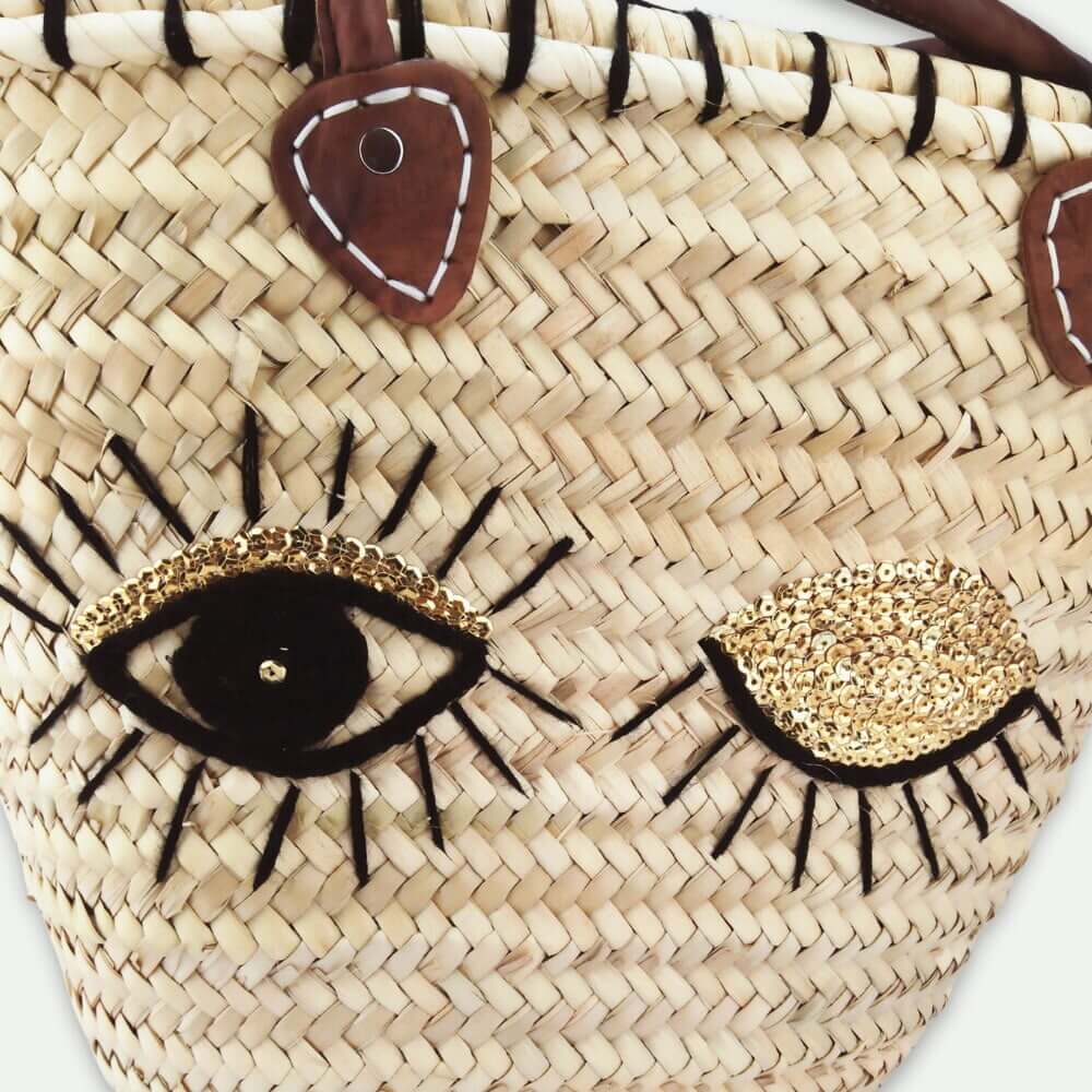 Moroccan straw tote bag with black and gold evil eye design and leather handles