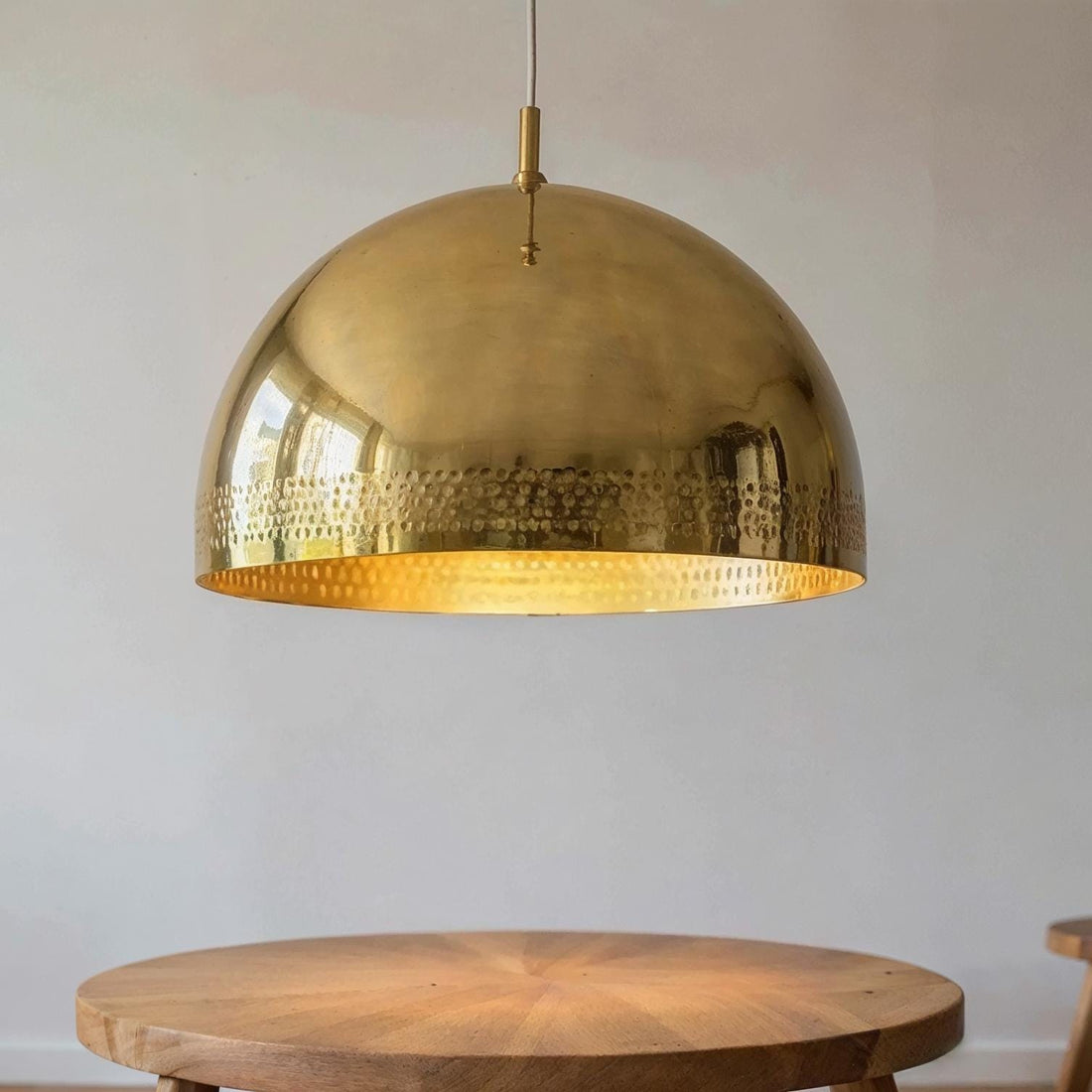 Polished brass dome pendant light with subtle hammered detailing above a wooden dining table