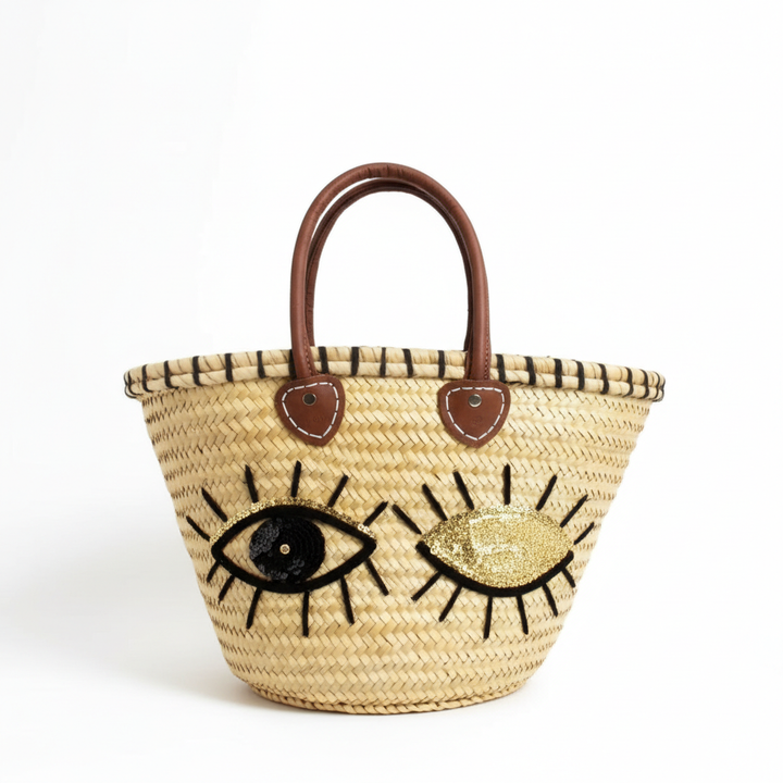 Moroccan straw tote bag with black and gold evil eye design and leather handles